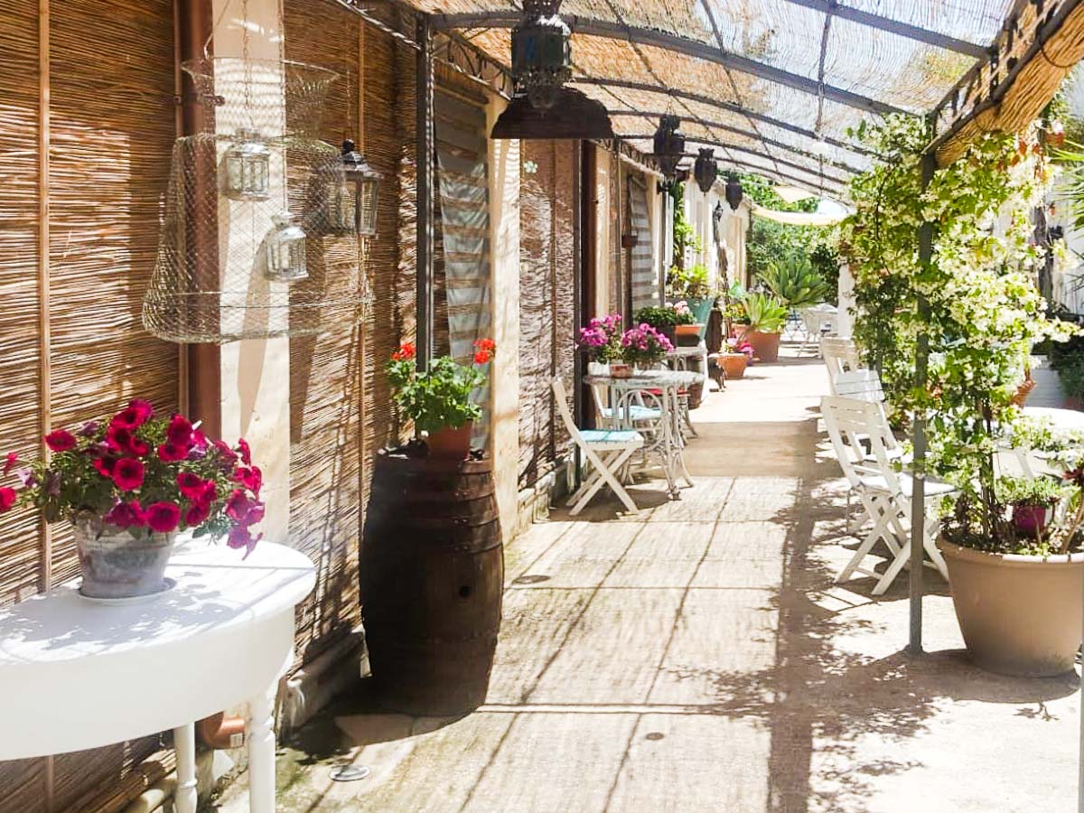 Veranda ombreggiata dell’agriturismo A Lumia con sedie bianche e fiori colorati